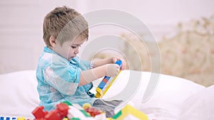 Child playing with colorful toy blocks. Kids play. Little boy building tower of block toys sitting on bed in white