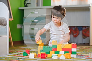 Child playing with colorful toy blocks. Little boy building tower at home or day care. Educational toys for young children.