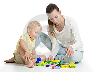 Child playing with colourful block toys on floor, isolated on white. Mother helps to son