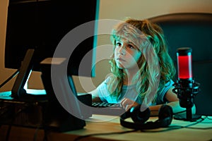 Child playing computer games or studying on pc computer. Kid gamer on night neon lighting. Little hacker, young