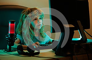 Child playing computer games or studying on pc computer. Kid gamer on night neon lighting. Little hacker, young