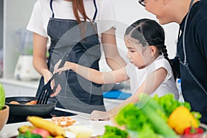 Child playing cook food with father and mother at home kitchen. Asian family happiness moment together photo