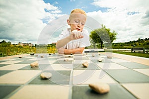 Child playing draughts or checkers board game outdoor