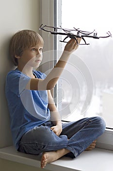 Child playing with drone. Boy sitting on window sill and holding quadrocopter in his hand. Technology, leisure toys