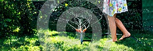 Child playing with garden sprinkler. Girl running, jumping. Lifestyle, authentic concept. Banner