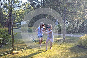 Child playing with garden sprinkler. Kids run and jump. Summer outdoor water fun in the backyard