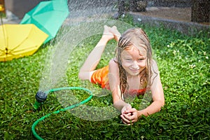 Child playing with garden sprinkler. Summer outdoor water fun in backyard. Ggirl play with hose watering grass. Kid