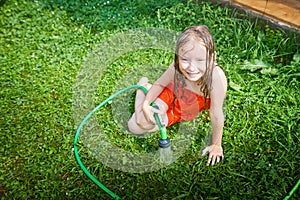 Child playing with garden sprinkler. Summer outdoor water fun in backyard. Ggirl play with hose watering grass. Kid