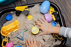 Child playing with kinetic sand and toy construction machinery. Hand of child in sand close up. Flat lay, top view. Indoor Table