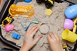 Child playing with kinetic sand and toy construction machinery. Hand of child in sand close up. Flat lay, top view. Indoor Table