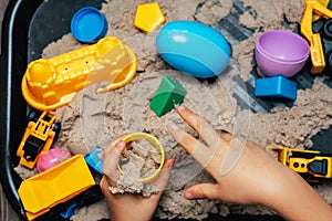 Child playing with kinetic sand and toy construction machinery. Hand of child in sand close up. Flat lay, top view. Indoor Table