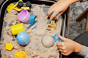 Child playing with kinetic sand and toy construction machinery. Hand of child in sand close up. Flat lay, top view. Indoor Table