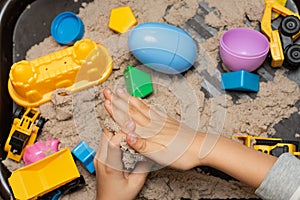 Child playing with kinetic sand and toy construction machinery. Hand of child in sand close up. Flat lay, top view. Indoor Table