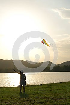 Child playing with a kite while running on a meadow by the lake at sunset. Healthy summer activity for children. Funny time with