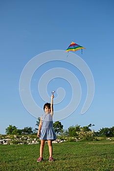 Child playing with a kite while running on a meadow by the lake at sunset. Healthy summer activity for children. Funny time with