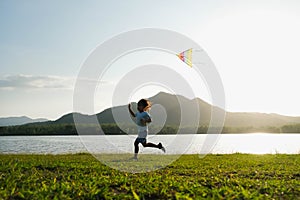 Child playing with a kite while running on a meadow by the lake at sunset. Healthy summer activity for children. Funny time with