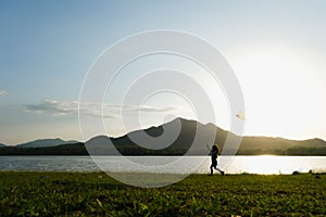 Child playing with a kite while running on a meadow by the lake at sunset. Healthy summer activity for children. Funny time with