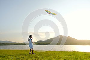 Child playing with a kite while running on a meadow by the lake at sunset. Healthy summer activity for children. Funny time with