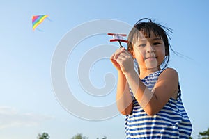 Child playing with a kite while running on a meadow by the lake at sunset. Healthy summer activity for children. Funny time with