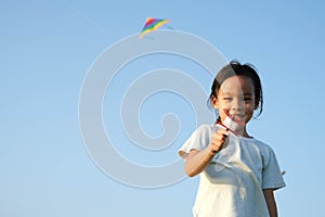 Child playing with a kite while running on a meadow by the lake at sunset. Healthy summer activity for children. Funny time with