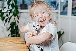 child playing with little cat. A little girl holds a white kitten. A little girl snuggles up to a cute pet and smiles while photo