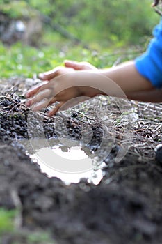 Child playing with mud - blur hands for focus on pond
