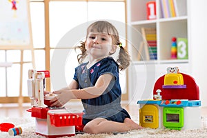 Child playing in nursery with educational toys. Toddler kid in a playroom. Little girl cooking in toy kitchen.