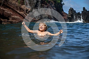 Child playing in ocean water. Kid jumping in the sea waves. Kids vacation on beach. Little excited boy swimming during