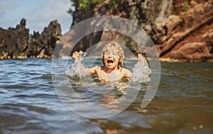 Child playing in ocean water. Kid jumping in the sea waves. Kids vacation on beach. Little excited boy swimming during