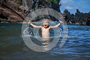 Child playing in ocean water. Kid jumping in the sea waves. Kids vacation on beach. Little excited boy swimming during