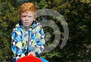 Child playing on outdoor playground. Boy play on school or kindergarten yard. Kid with curly ginger hair. Portrait. The