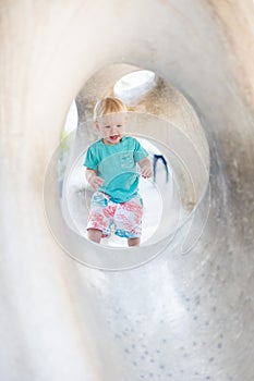 Child playing on outdoor playground. Toddler plays on school or kindergarten yard. Active kid on stone sculpured slide