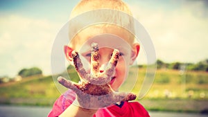 Child playing outdoor showing dirty muddy hands.