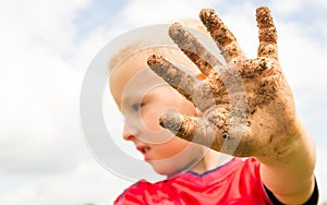 Child playing outdoor showing dirty muddy hands.