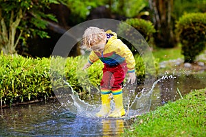 Child playing in puddle. Kids jump in autumn rain