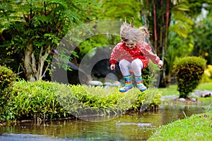 Child playing in puddle. Kids jump in autumn rain