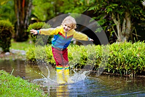 Child playing in puddle. Kids jump in autumn rain