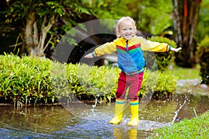 Child playing in puddle. Kids jump in autumn rain