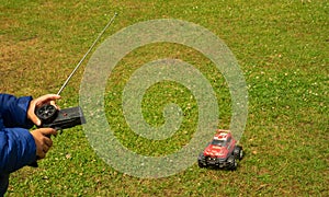 A child is playing with a radio-controlled typewriter. A little racing driver. Radio-controlled red car on green grass