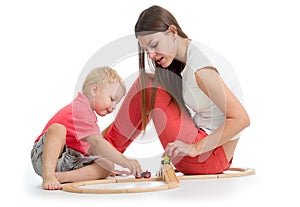 Child playing with railway toys on floor, isolated on white. Mother helps to son