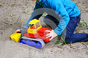 A child playing on the sand with a toy car.