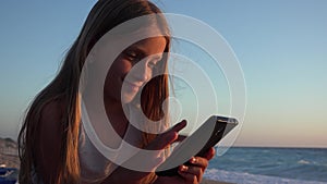 Child playing smartphone, kid on beach at sunset, girl using tablet on seashore