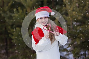 Child playing in snow on Christmas vacation. Winter outdoor fun. Kids play in snowy park on Xmas eve. Little girl in Santa hat,