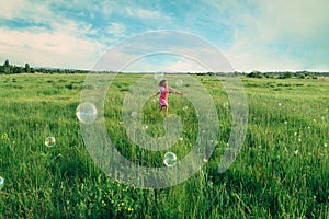 Child playing among soap bubbles in summer