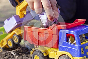 The child is playing in the street with sand; he loads the earth in an dump truck toy