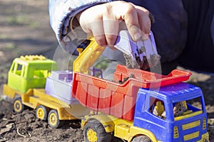 The child is playing in the street with sand; he loads the earth in an dump truck toy