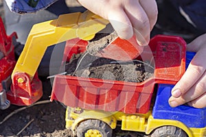 The child is playing in the street with sand; he loads the earth in an dump truck toy photo