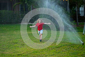 Child playing at summer backyard. Water fun in garden. Kid play with water sprinkler in garden. Funny little boy playing