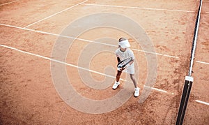 Child playing tennis on outdoor clay court. Top view of little tennis player on open tennis court. Full length shot of sporty