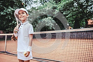 Child playing tennis on outdoor court. Little girl with tennis racket and ball in sport club